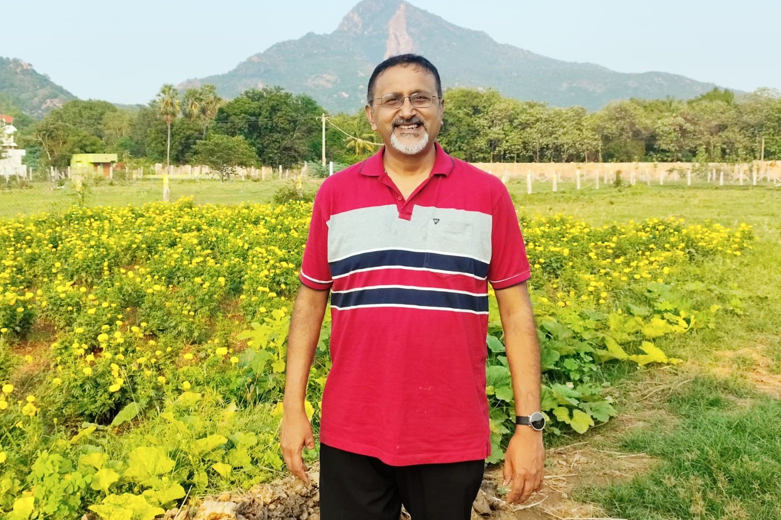 Shankar Venkatraman standing in a marigold field with hills behind